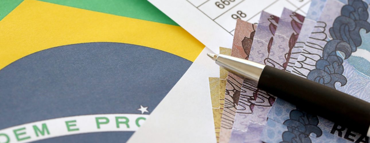 Pen with Brazilian money bills on flag of Brazil republic. Concept of business, accounting or taxpaying in Brazil
